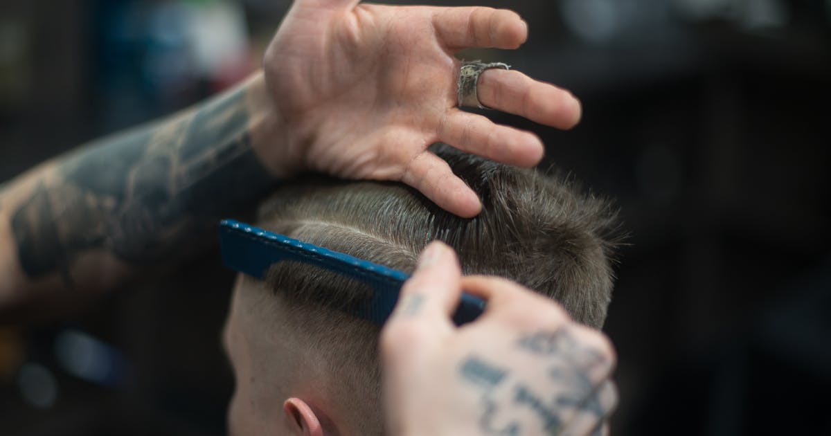 Barbero peinando y dando forma al cabello de un hombre en la barbería